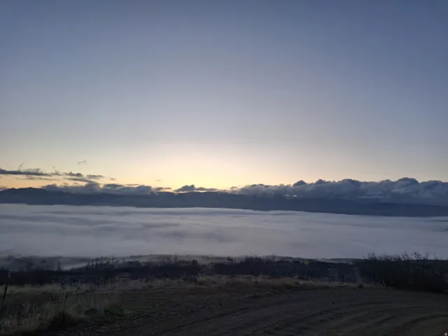 Expansive natural landscape featuring rolling hills, distant mountains, and a prominent fog layer