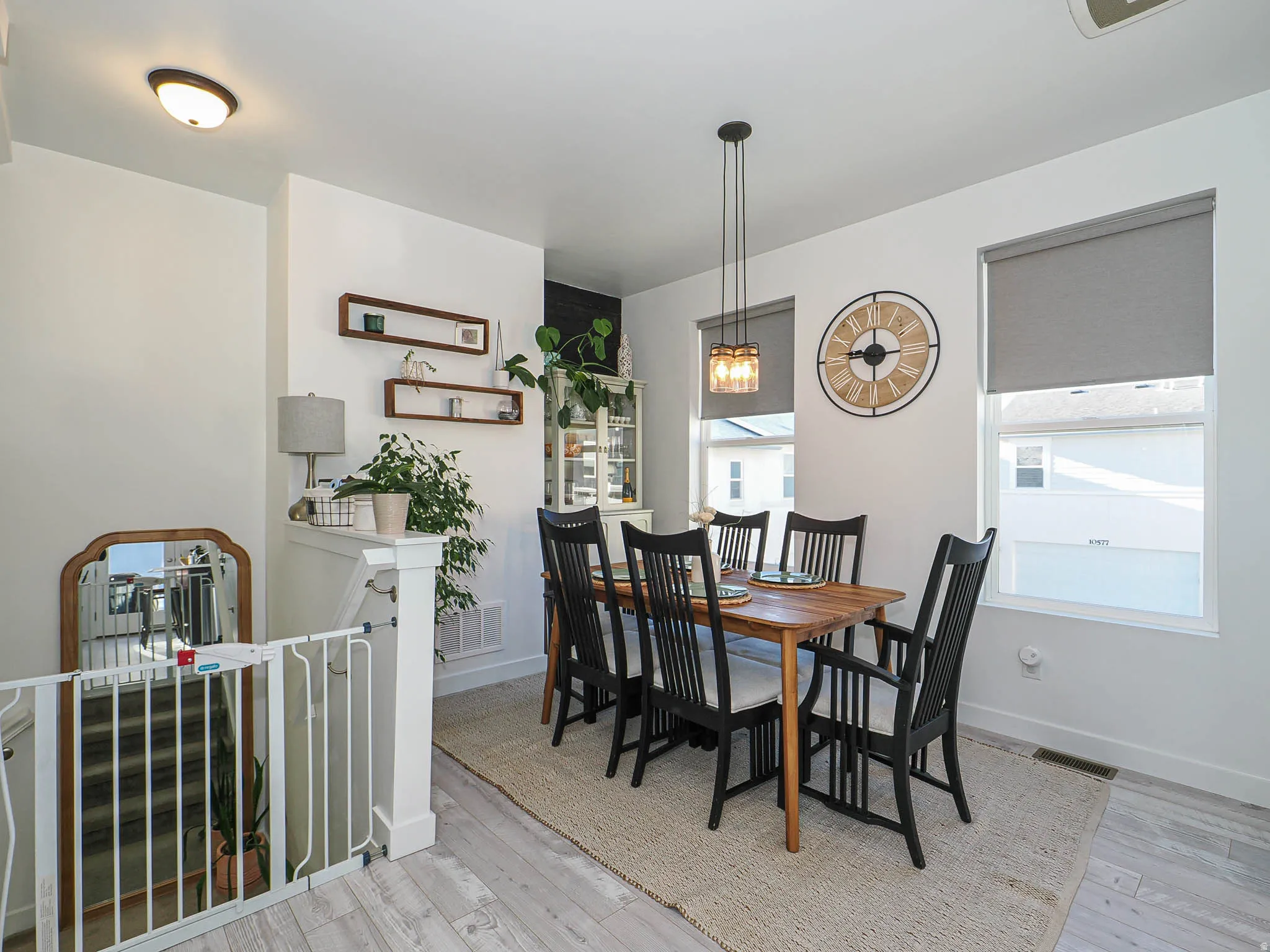 Dining area featuring wood-finish flooring, two large windows with roller shades, and a multi-pendant ceiling light fixture