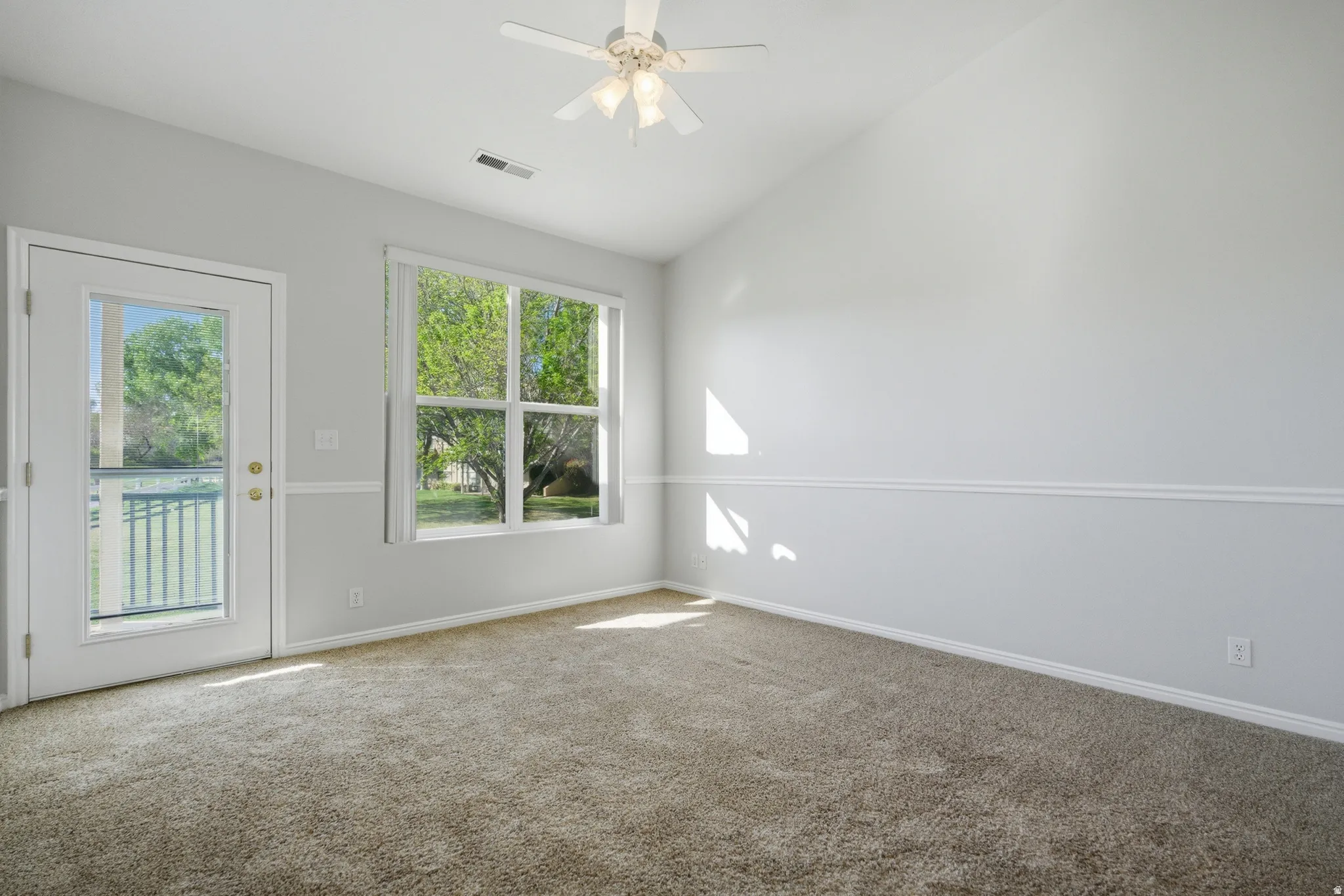 Spacious room featuring vaulted ceilings, plush carpet flooring, and a ceiling fan