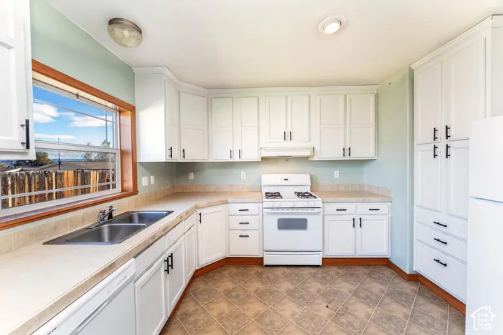 Kitchen featuring white shaker-style cabinetry with matte black hardware, laminate countertops, a dual-basin stainless steel sink, and ceramic tile flooring