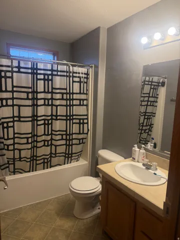 Full bathroom featuring a white tub, toilet, and wood-finish vanity with an integrated sink and light-toned countertop