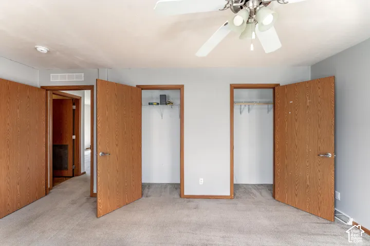 Room interior featuring neutral wall paint, carpeting, a ceiling fan with integrated lighting, and two closets with wood-finish doors