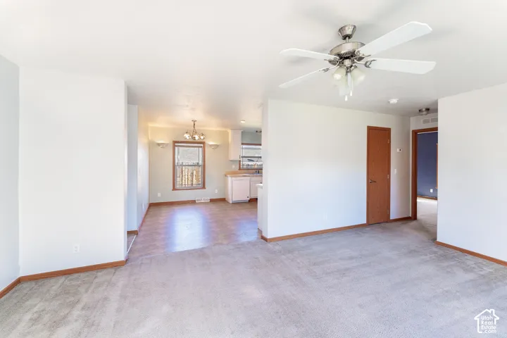 Open-concept interior featuring wall-to-wall carpeting, a ceiling fan with multi-light fixture, wood-finished interior doors, and a multi-light chandelier