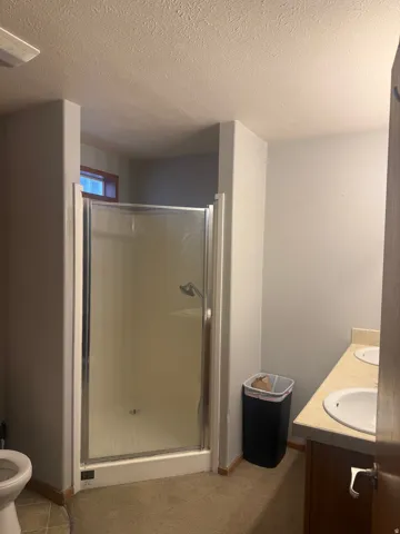 Shower enclosure with chrome frame, dual vanity with undermount sinks, light-colored countertop, and wood-finish cabinetry