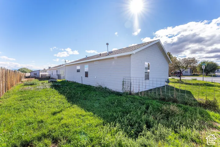 Exterior featuring light-colored horizontal siding, asphalt shingle roofing, wire perimeter fencing, and open lot space