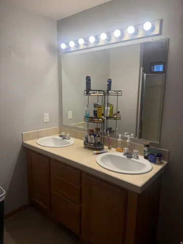 Spacious bathroom vanity featuring dual sinks with individual faucets, ample countertop space, and a large mirror with integrated vanity lighting