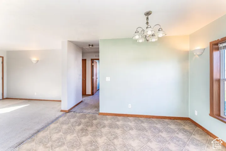 Multi-textured flooring including neutral carpeting and diamond-patterned tile, multi-arm chandelier, wall-mounted sconce lighting, and wood-trim window casings