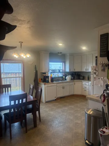 Open-concept kitchen and dining area featuring white cabinetry with silver hardware, light-toned countertops, and an integrated dishwasher