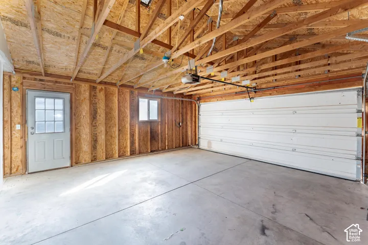 Multi-car garage featuring exposed wood framing, concrete flooring, a paneled metal garage door, and a dedicated exterior side door