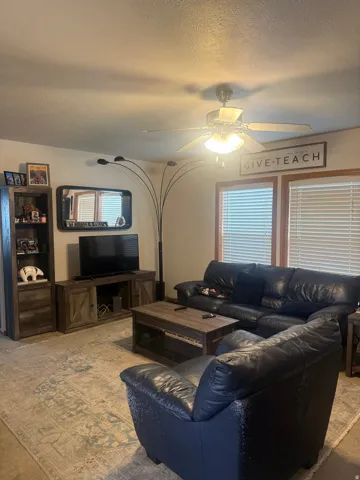 Living area featuring a ceiling fan with integrated lighting, wood-finish window frames, and horizontal blinds