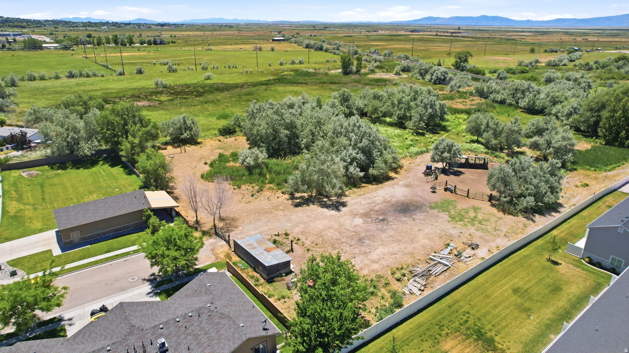 Expansive undeveloped lot featuring scattered mature trees, a fenced paddock area, and a storage shed