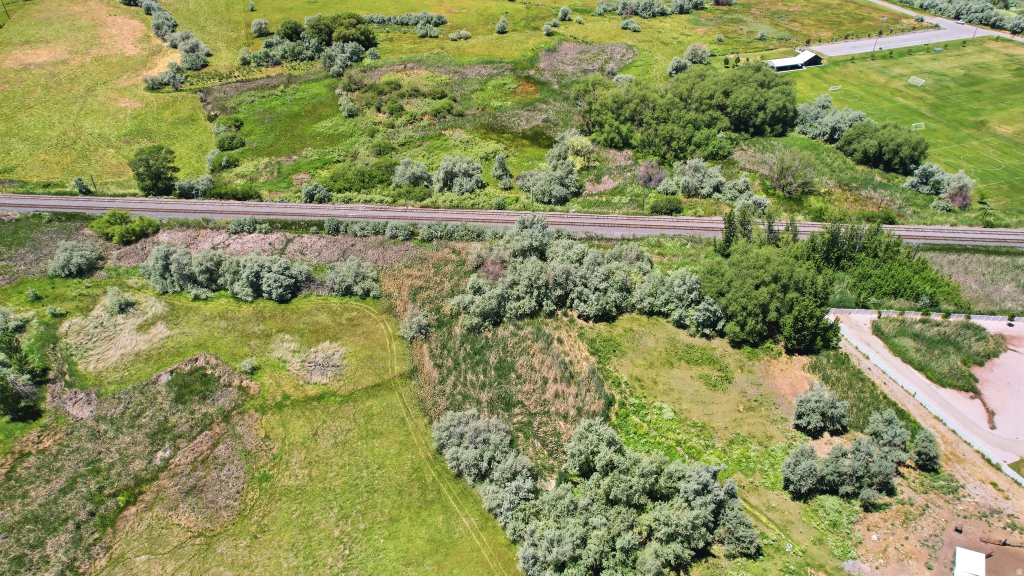Expansive acreage featuring abundant natural greenery, a visible railroad track, and a section of paved road