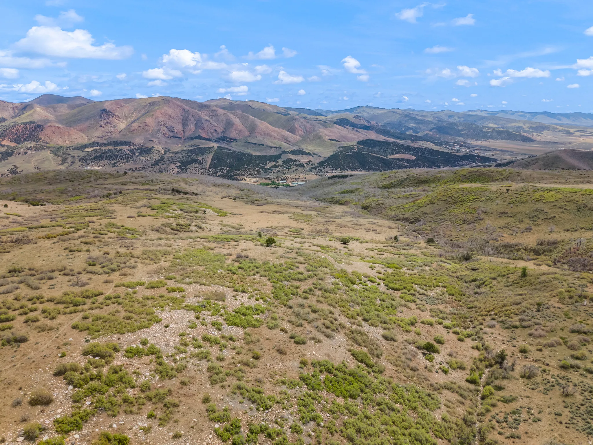Expansive open terrain featuring natural brush and distant mountain ranges under a partly cloudy sky