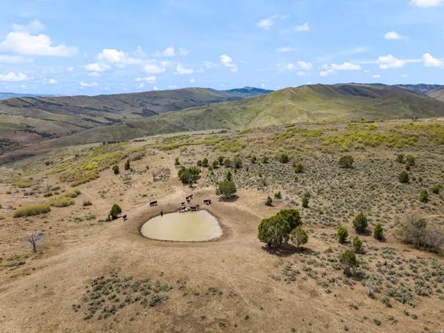 Expansive high desert landscape featuring rolling hills and a natural water source