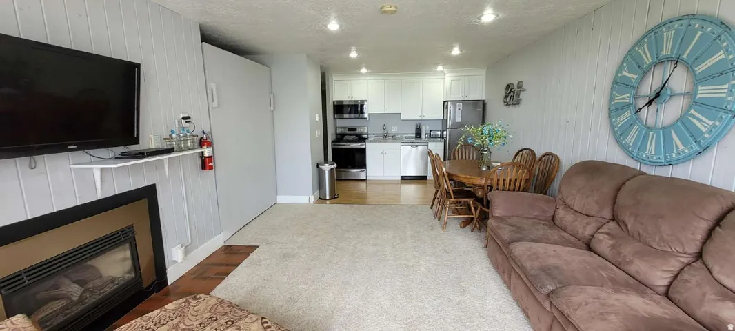 Open concept living area featuring a fireplace, carpet flooring, recessed lighting, and a kitchen with white cabinetry and stainless steel appliances