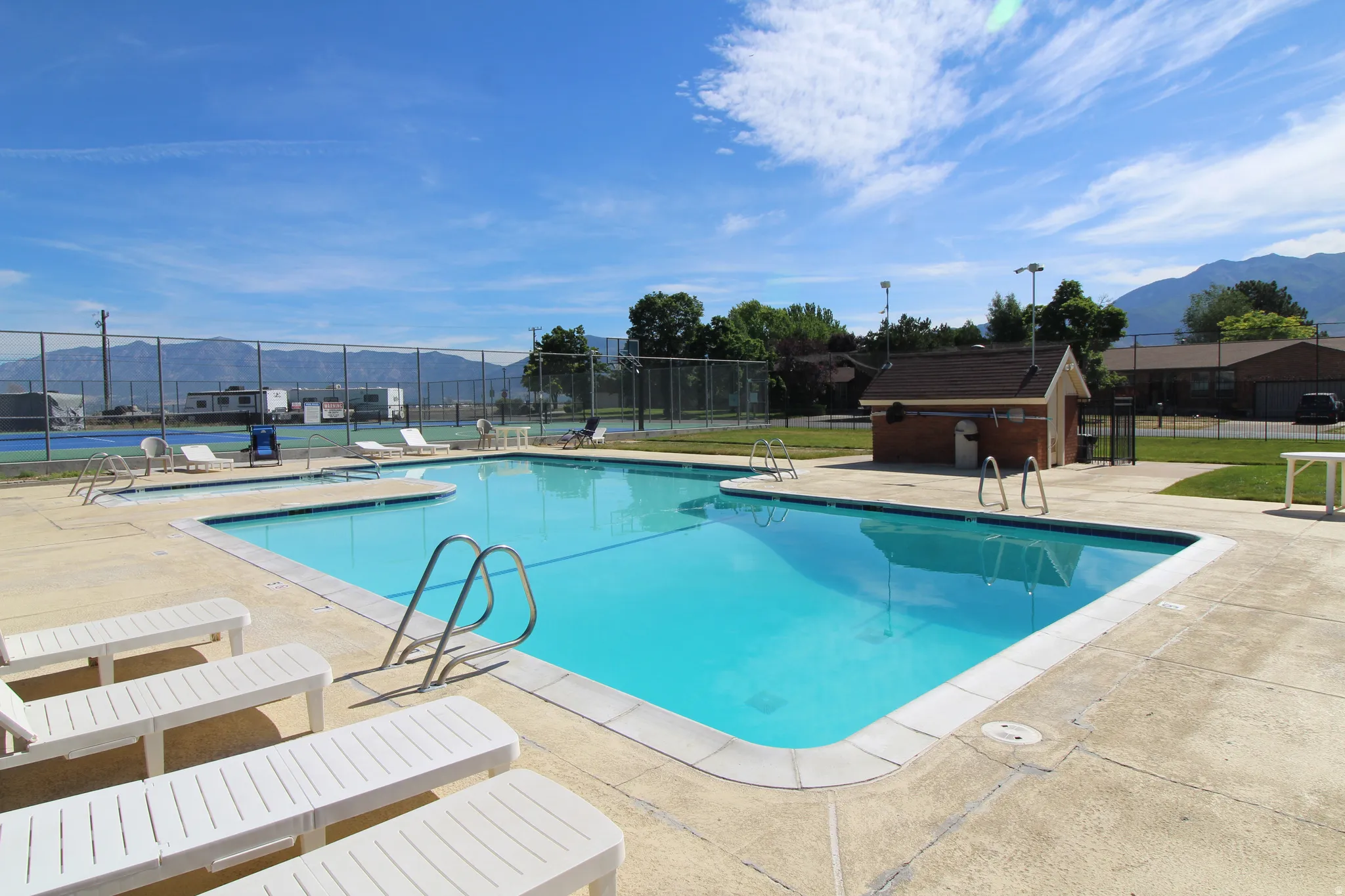 Outdoor swimming pool with concrete decking, perimeter fencing, and a nearby pickleball court