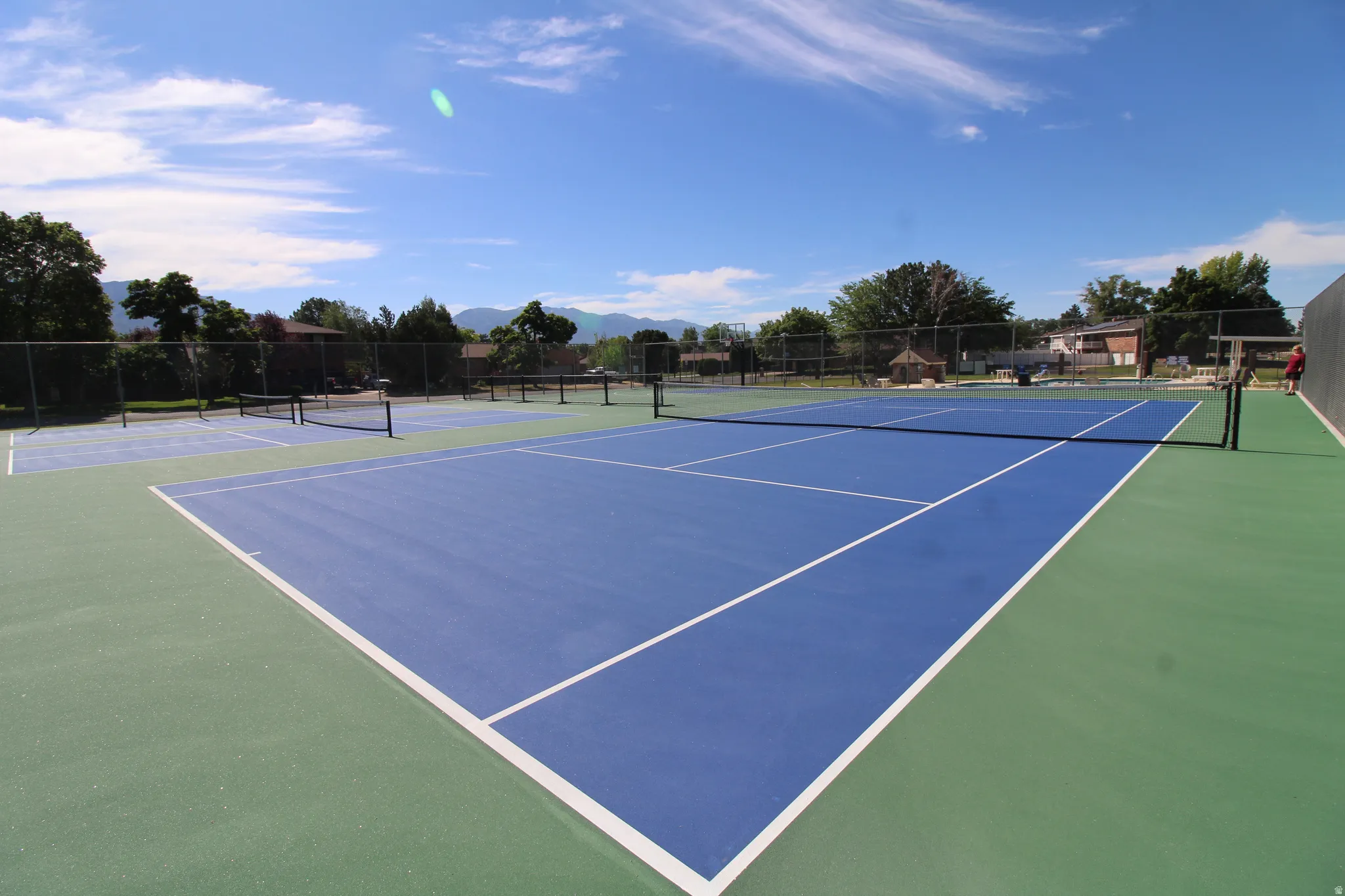 Recreational area featuring two full-size pickleball courts with blue and green surfacing, white line markings, and a black net