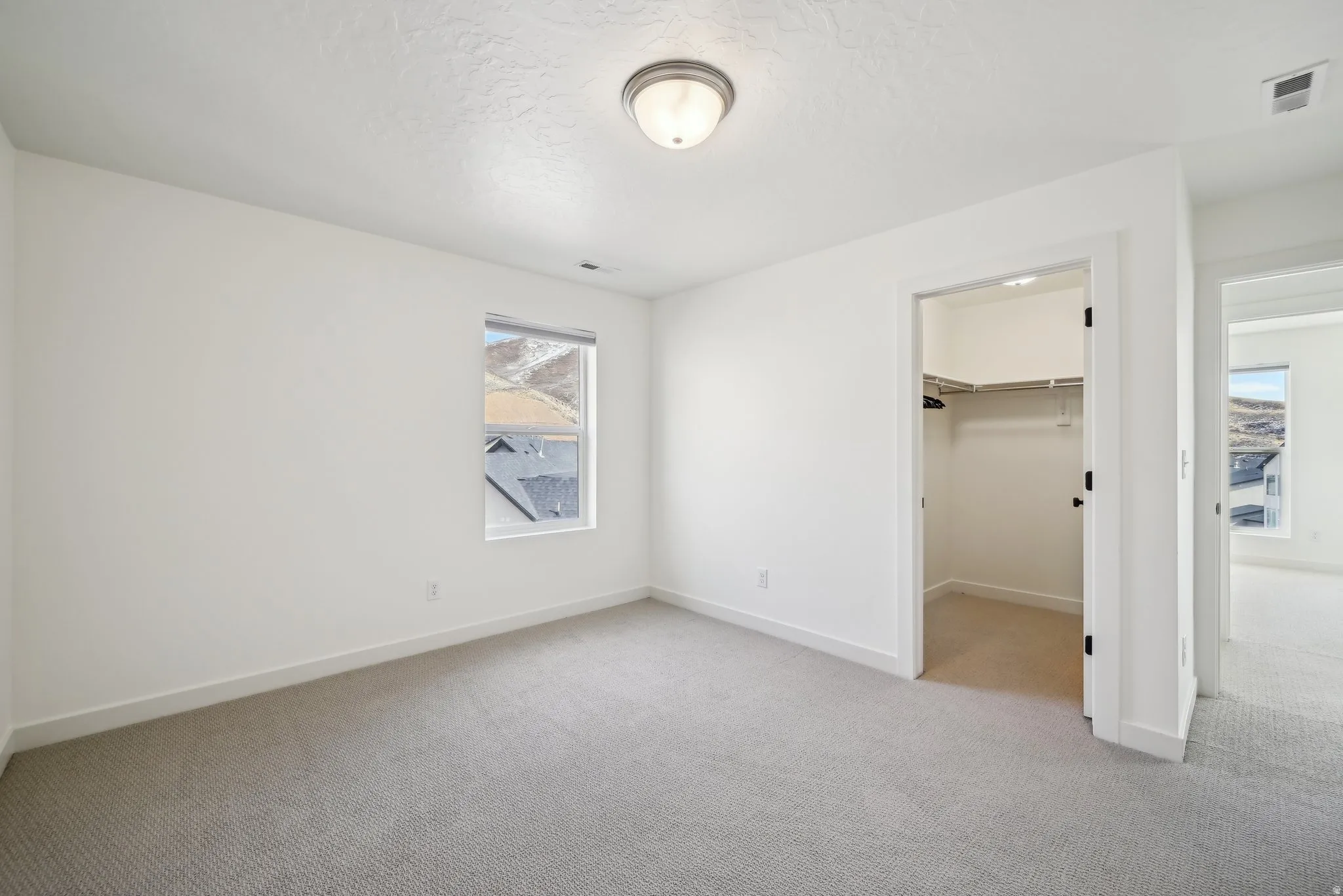 Bright interior room featuring neutral carpeting, white walls, and a window providing natural light