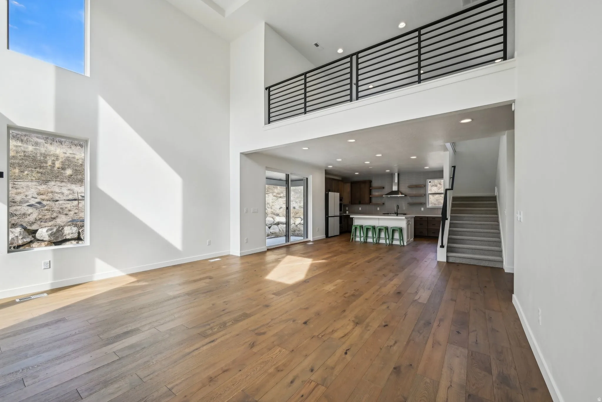 Open-concept living space featuring high ceilings, wood-finish flooring, and a second-story interior balcony with horizontal railings