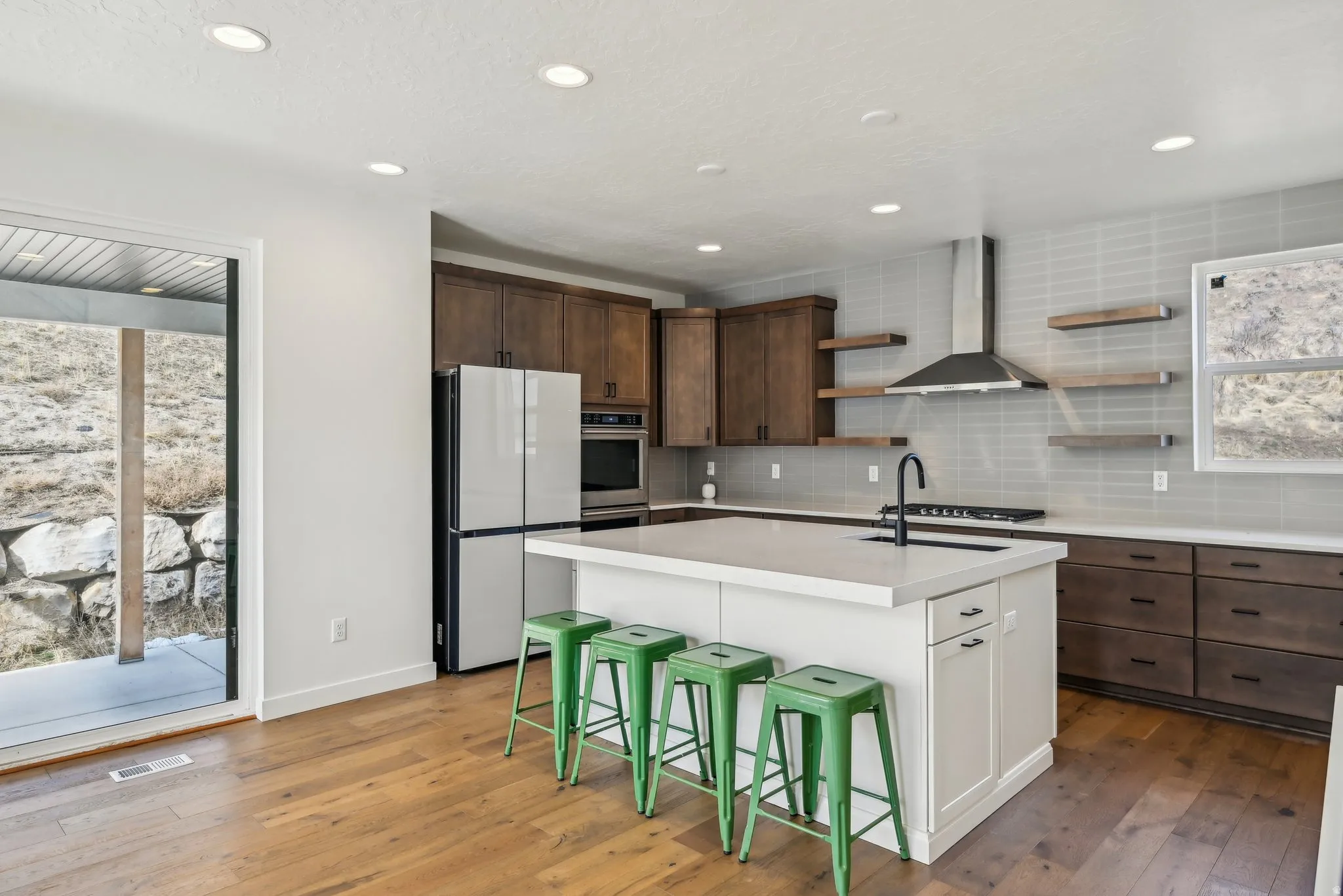 Modern kitchen featuring wood-finish flooring, a white countertop island, stainless steel appliances, dark wood cabinetry, and a tile backsplash