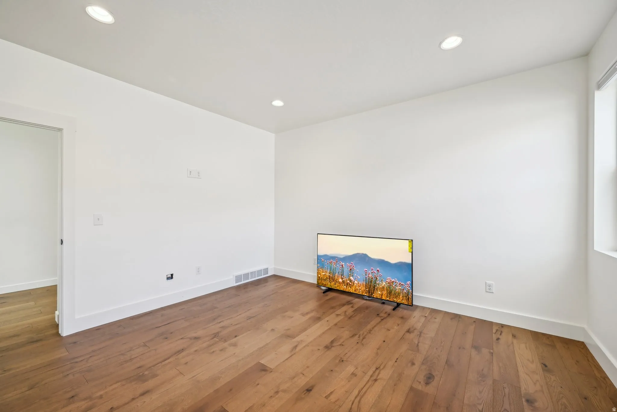 Spacious room featuring wood-finish flooring, recessed lighting, white walls, and white trim