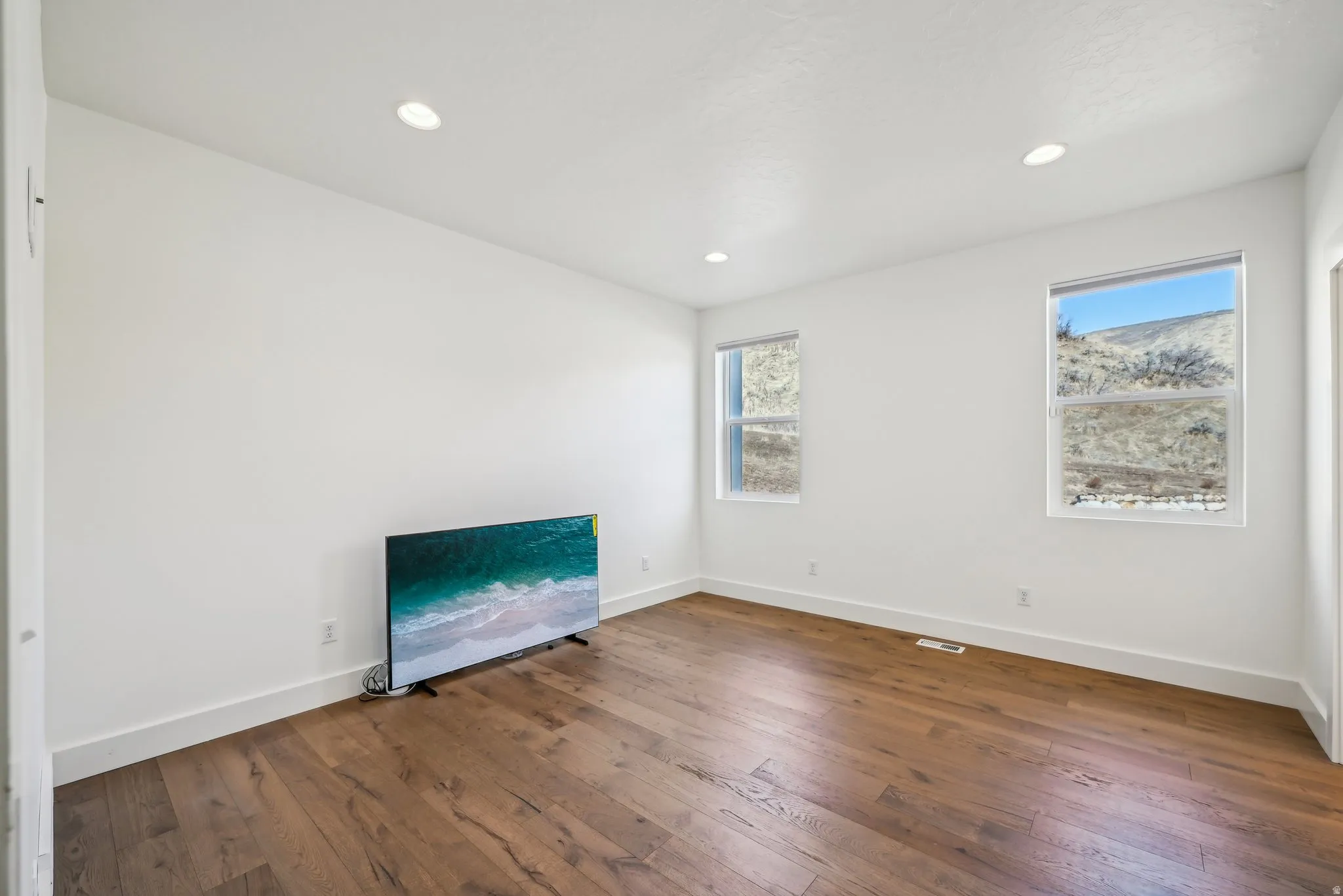Spacious room featuring wood-finish flooring, recessed lighting, and two large windows offering hillside scenery