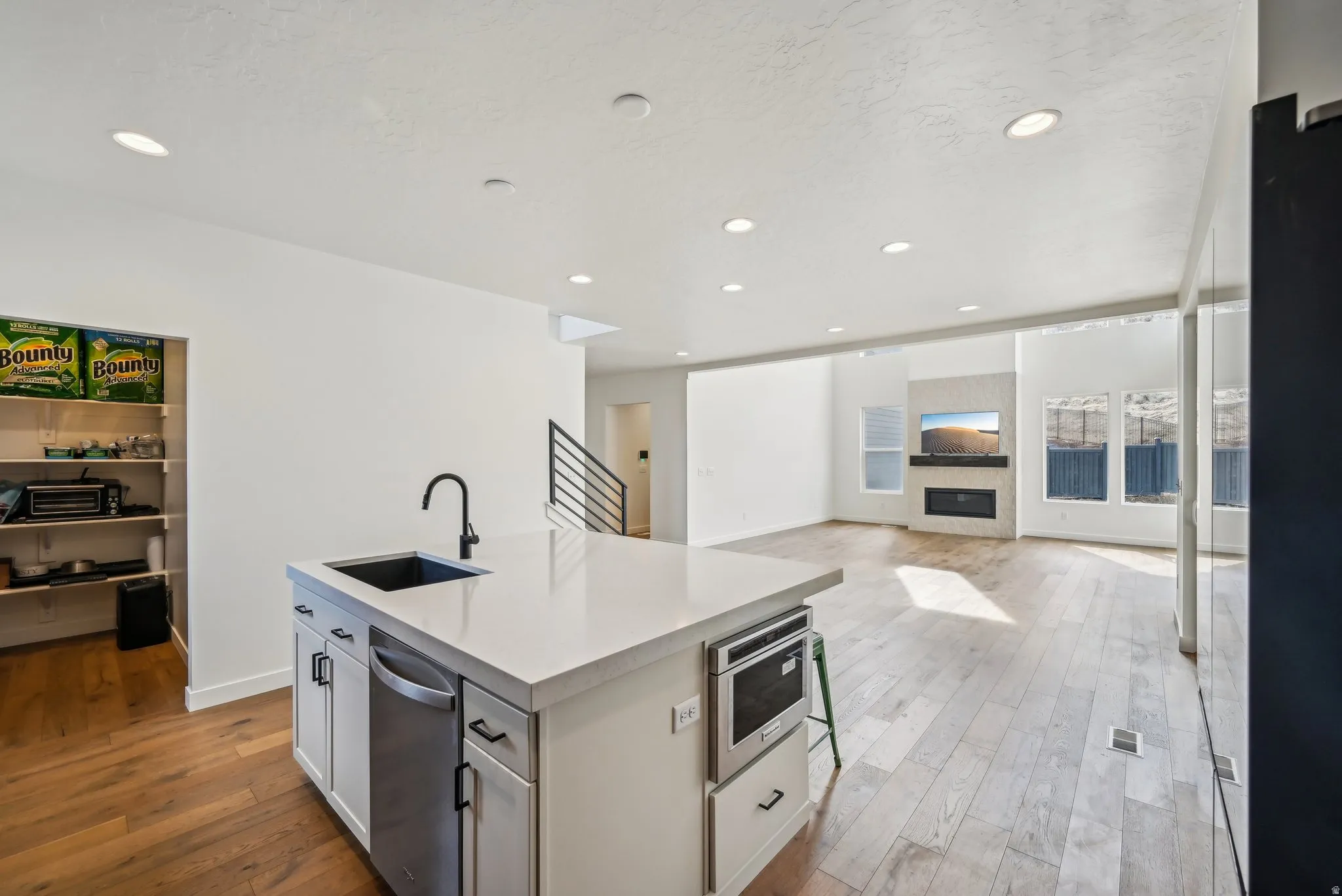 Open-concept living space featuring wood-finish flooring, a kitchen island with integrated sink and dishwasher, recessed lighting, and a contemporary fireplace with a built-in mantel
