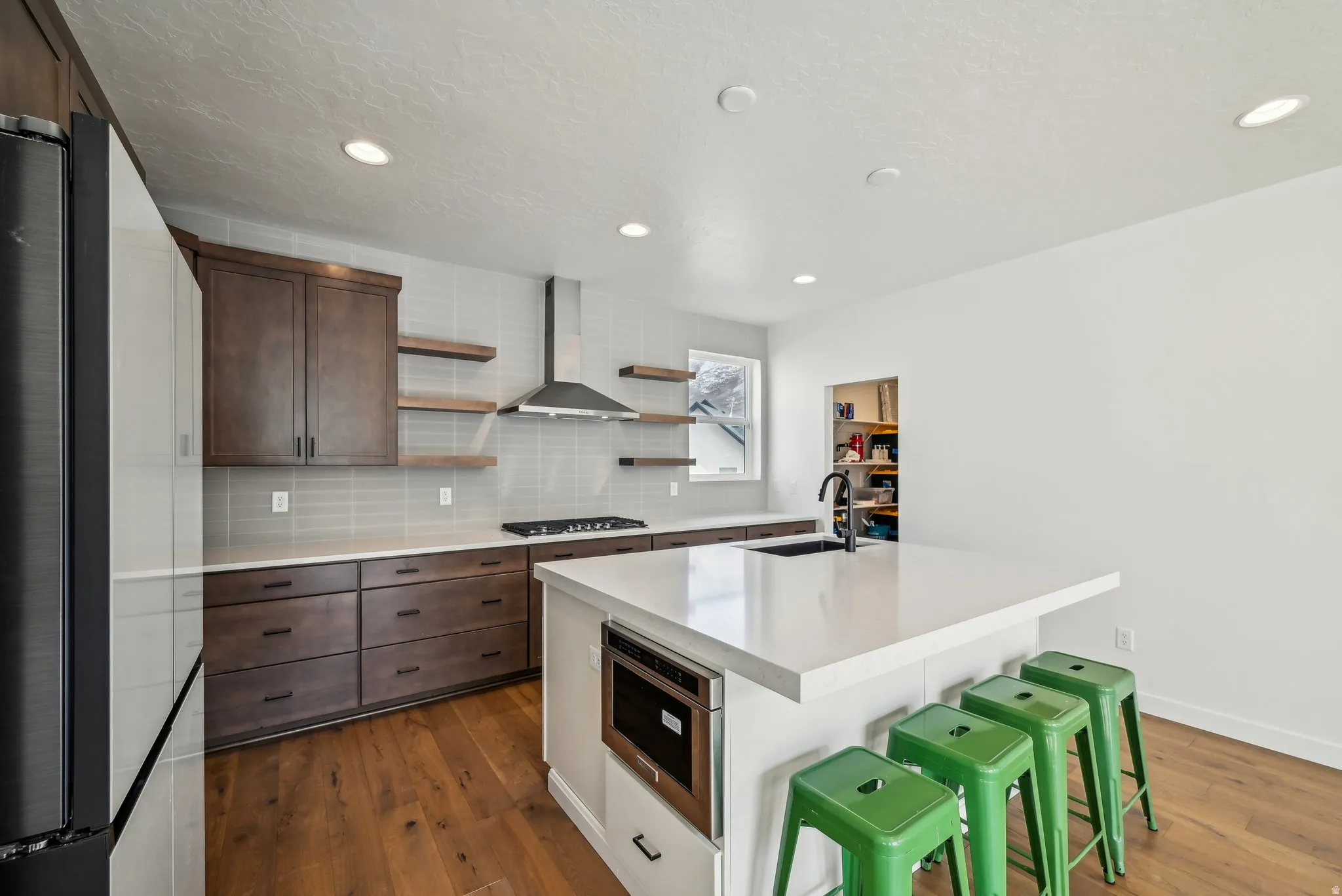 Contemporary kitchen featuring a large central island with integrated microwave, wood-finish flooring, dark wood cabinetry, and a subway tile backsplash