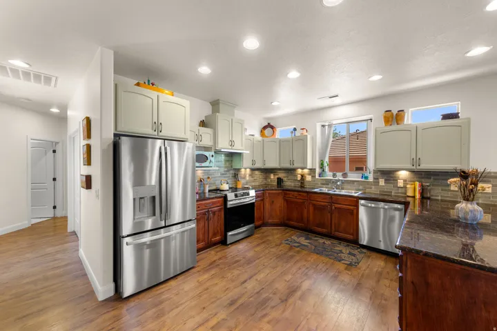 Kitchen featuring wood-finish flooring, stainless steel appliances, dark stone countertops, and a tile backsplash