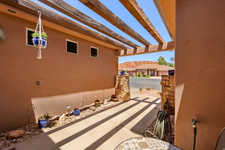 Covered patio featuring an open-beam pergola, stucco exterior, and stone-clad pillars