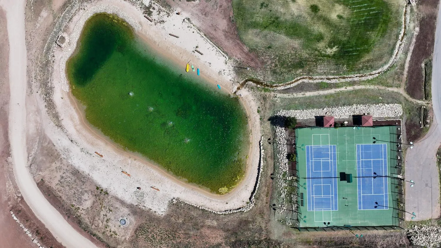 Outdoor recreational area featuring a large pond and two tennis courts