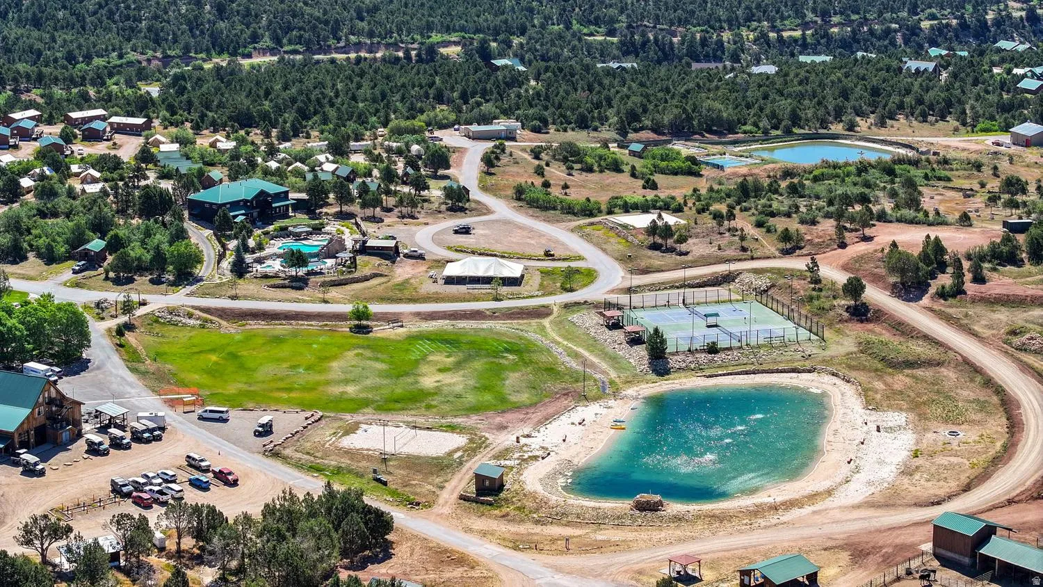Expansive property featuring multiple structures, a swimming pool, two tennis courts, and a pond with sandy edges