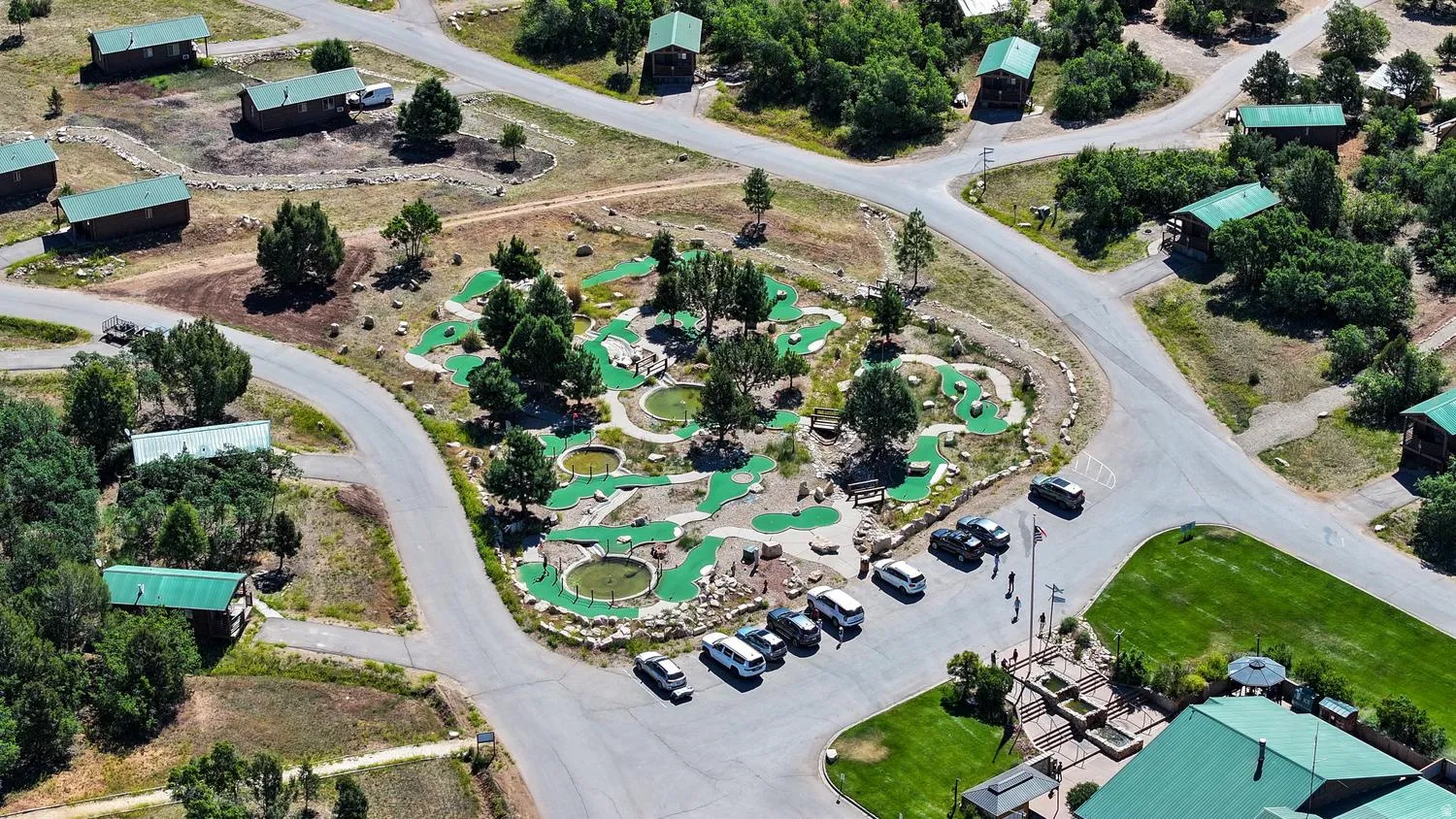 Miniature golf course with multiple greens, surrounded by established trees and paved pathways
