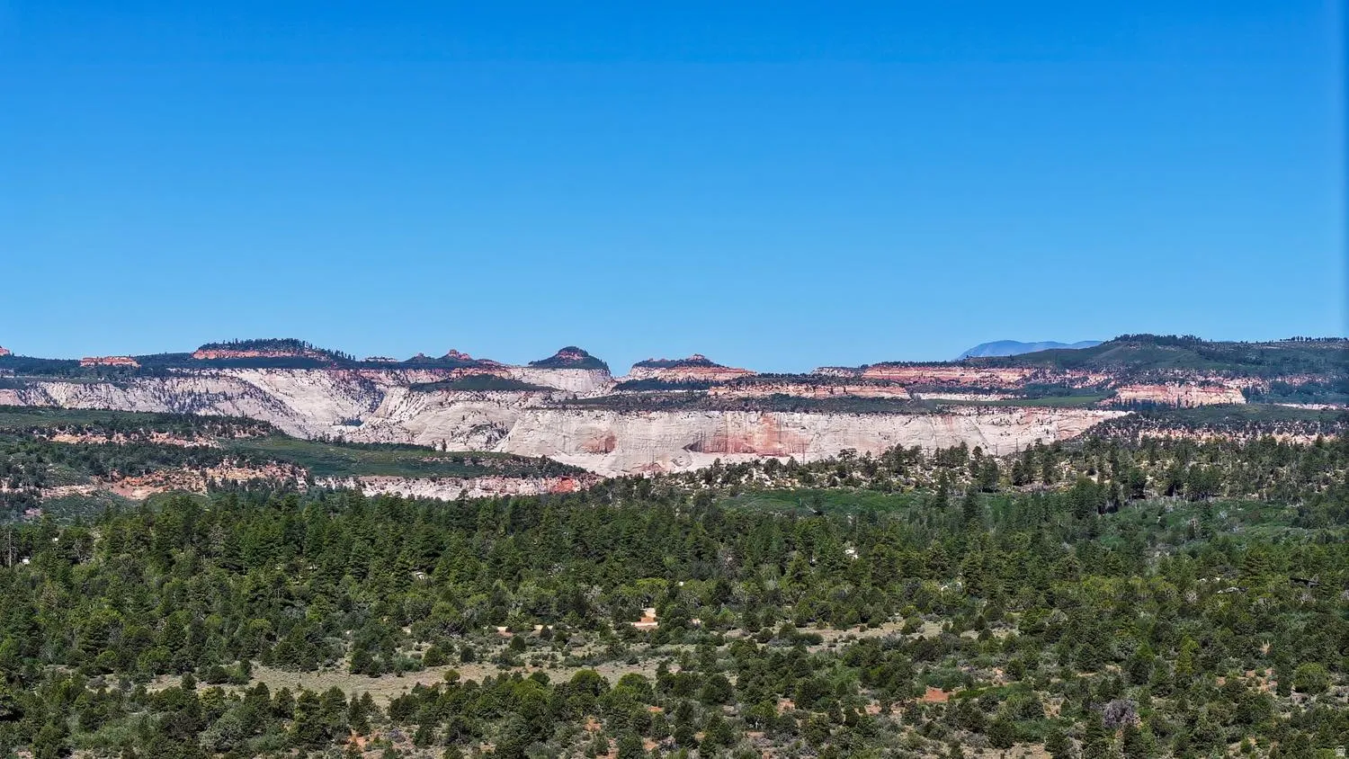 Expansive landscape featuring distant layered mountains and a dense foreground of green trees