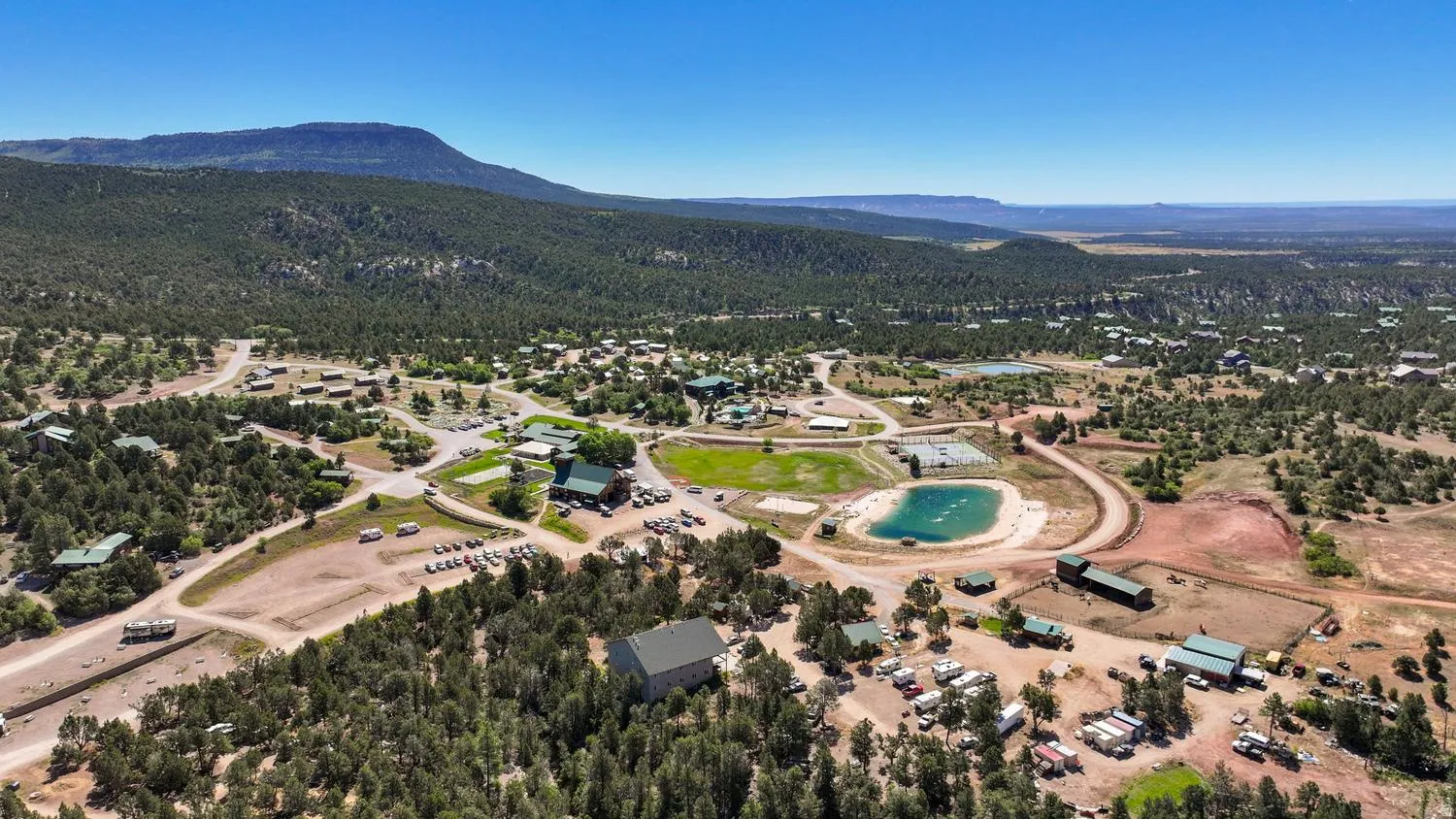 Expansive property featuring multiple structures, forested surroundings, open land, and a constructed pond