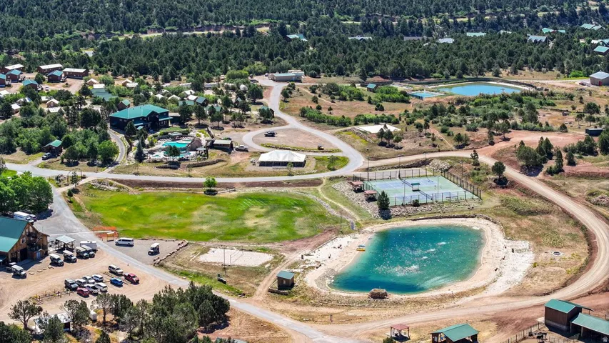 Expansive property featuring multiple structures, a swimming pool, two tennis courts, and a pond with sandy edges