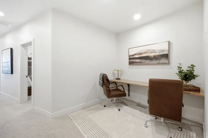 Dedicated workspace featuring a built-in wood-finish desk, recessed lighting, and soft carpeting