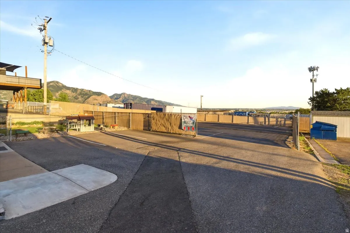 Paved parking area featuring a chain-link fence, a swing gate, and a distant mountain backdrop
