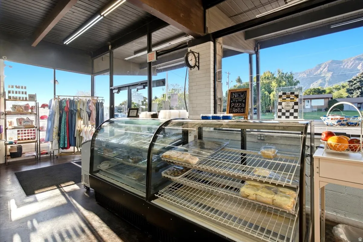 Commercial interior featuring a curved glass display case, exposed ceiling beams, concrete flooring, track lighting, and expansive storefront windows