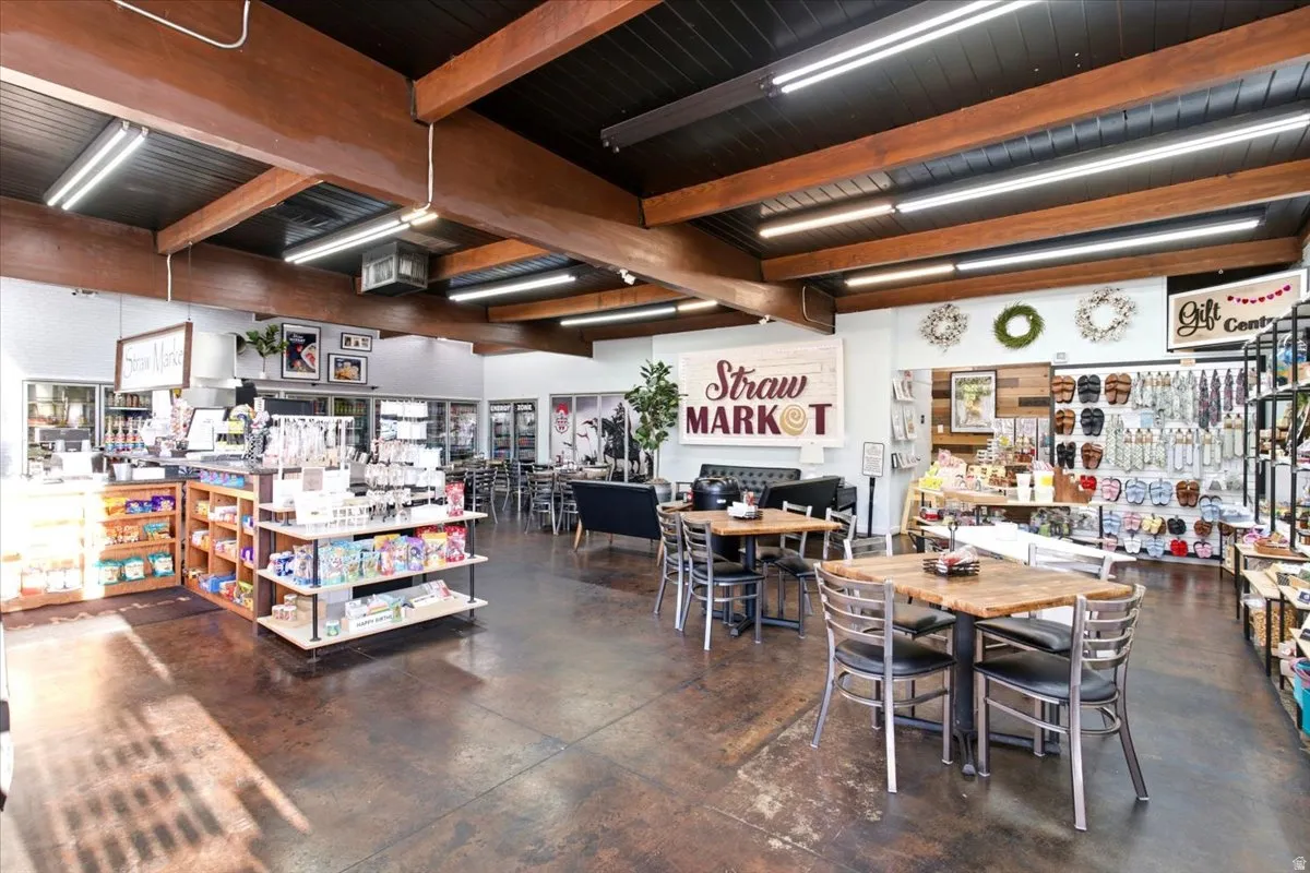 Open-concept retail space featuring exposed wood ceiling beams, a dark ceiling, linear fluorescent lighting, and stained concrete flooring