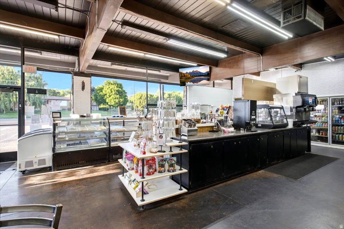 Retail space featuring a long service counter with integrated appliances, extensive display cases, expansive front windows, and exposed ceiling beams