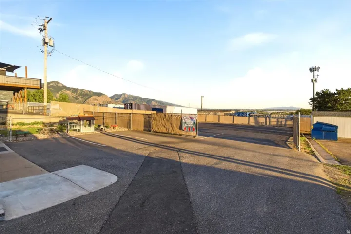 Paved parking area featuring a chain-link fence, a swing gate, and a distant mountain backdrop