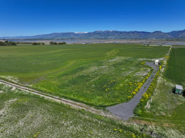 Expansive green acreage featuring a gravel access path, a white utility structure, a green storage shed, and distant mountain ranges