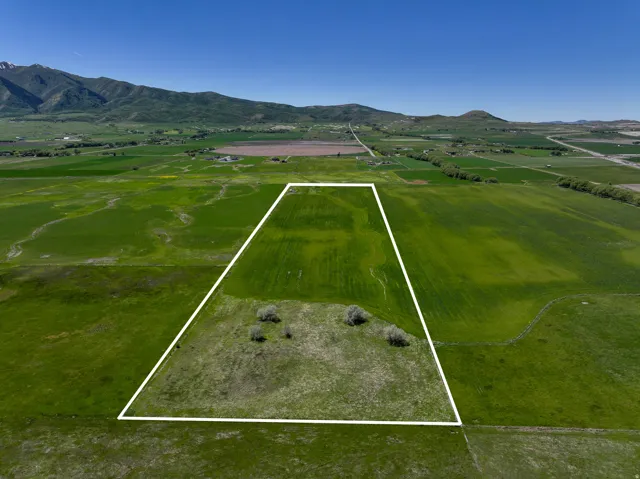 Expansive rural land parcel outlined in white, featuring varied green fields and distant mountain ranges under a clear sky