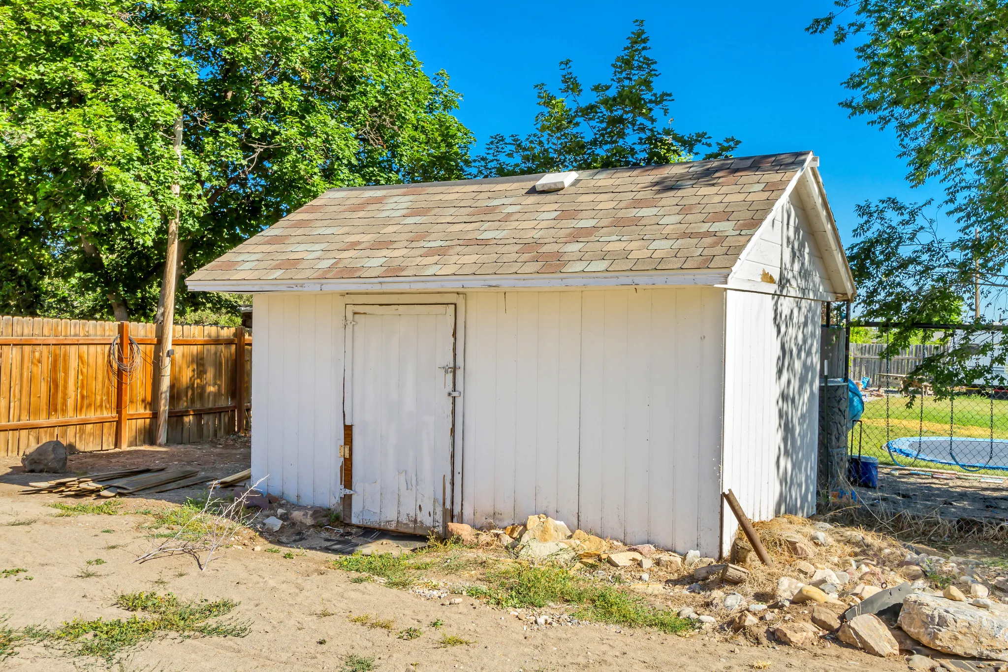 Freestanding storage shed featuring white siding and a brown shingle roof