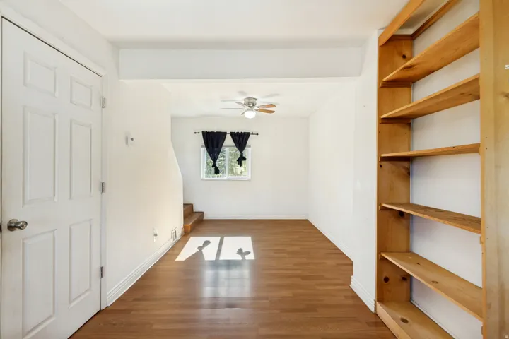 Open-plan living area featuring wood-finish flooring, a ceiling fan, and built-in wooden shelving