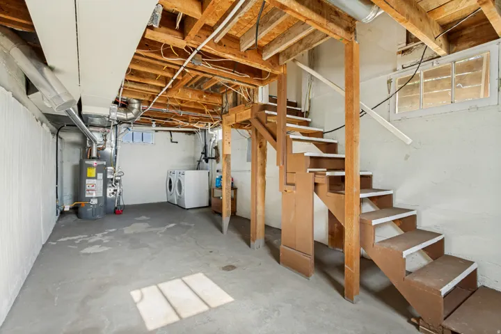 Spacious unfinished basement offering exposed wooden ceiling joists, concrete flooring, and a utilitarian water heater