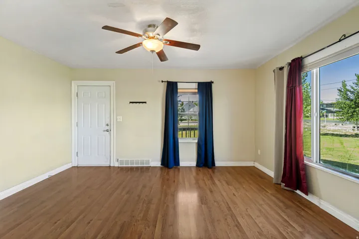 Spacious room featuring wood-finish flooring, light-toned walls, and a ceiling fan with integrated lighting