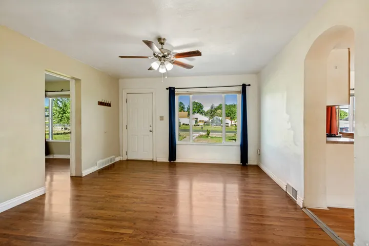 Spacious room featuring wood-finish flooring, a ceiling fan with light fixture, and a multi-pane window