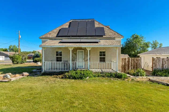 Brick exterior featuring a covered front porch with white railing, a shingled roof, and solar panels